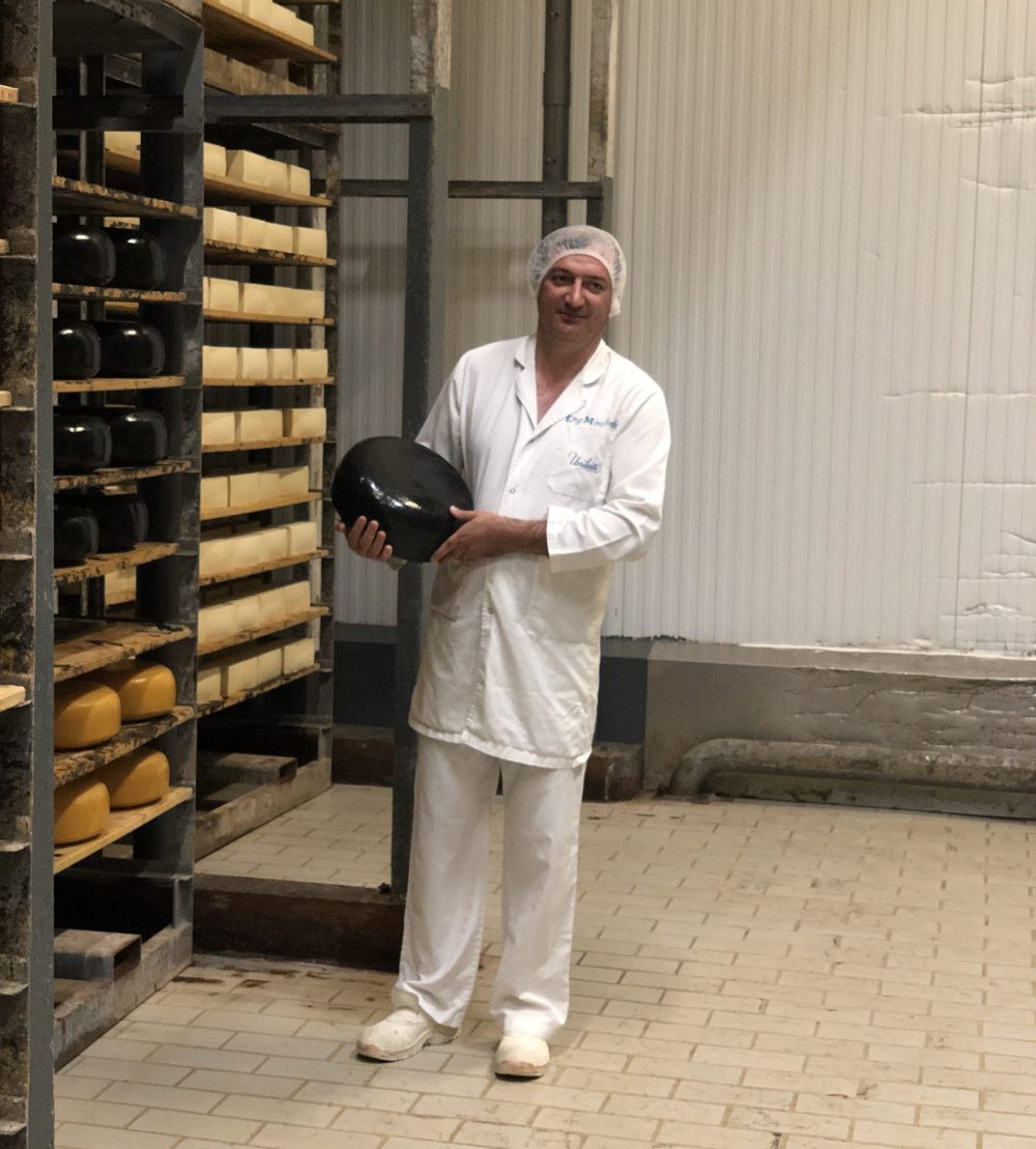 Fromager dans une usine tenant une meule de fromage à la peau noire