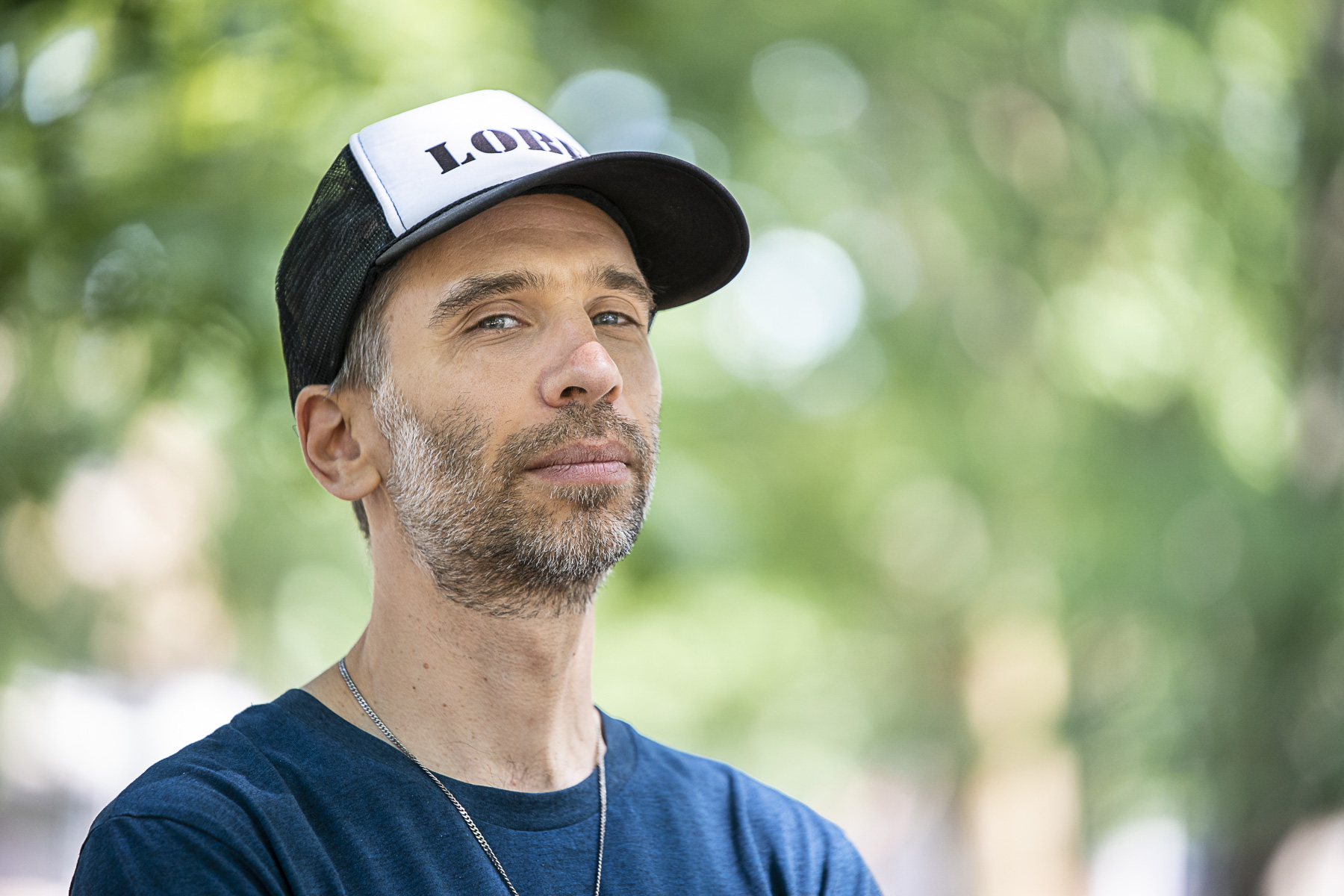 Le producteur et DJ Poirier portant une casquette devant un fond de verdure pour la sortie de son album Soft Power.