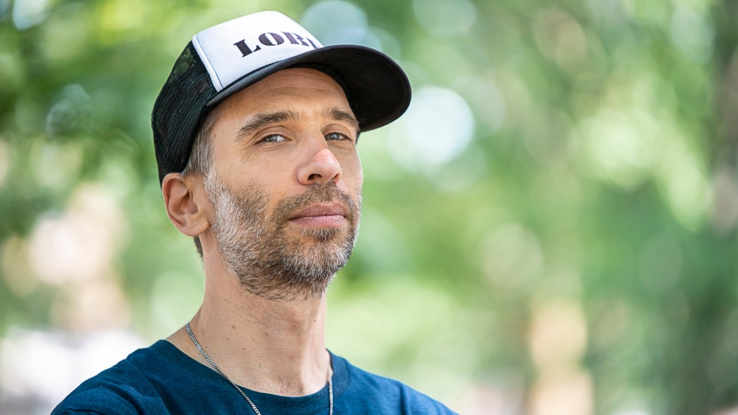 Le producteur et DJ Poirier portant une casquette devant un fond de verdure pour la sortie de son album Soft Power.