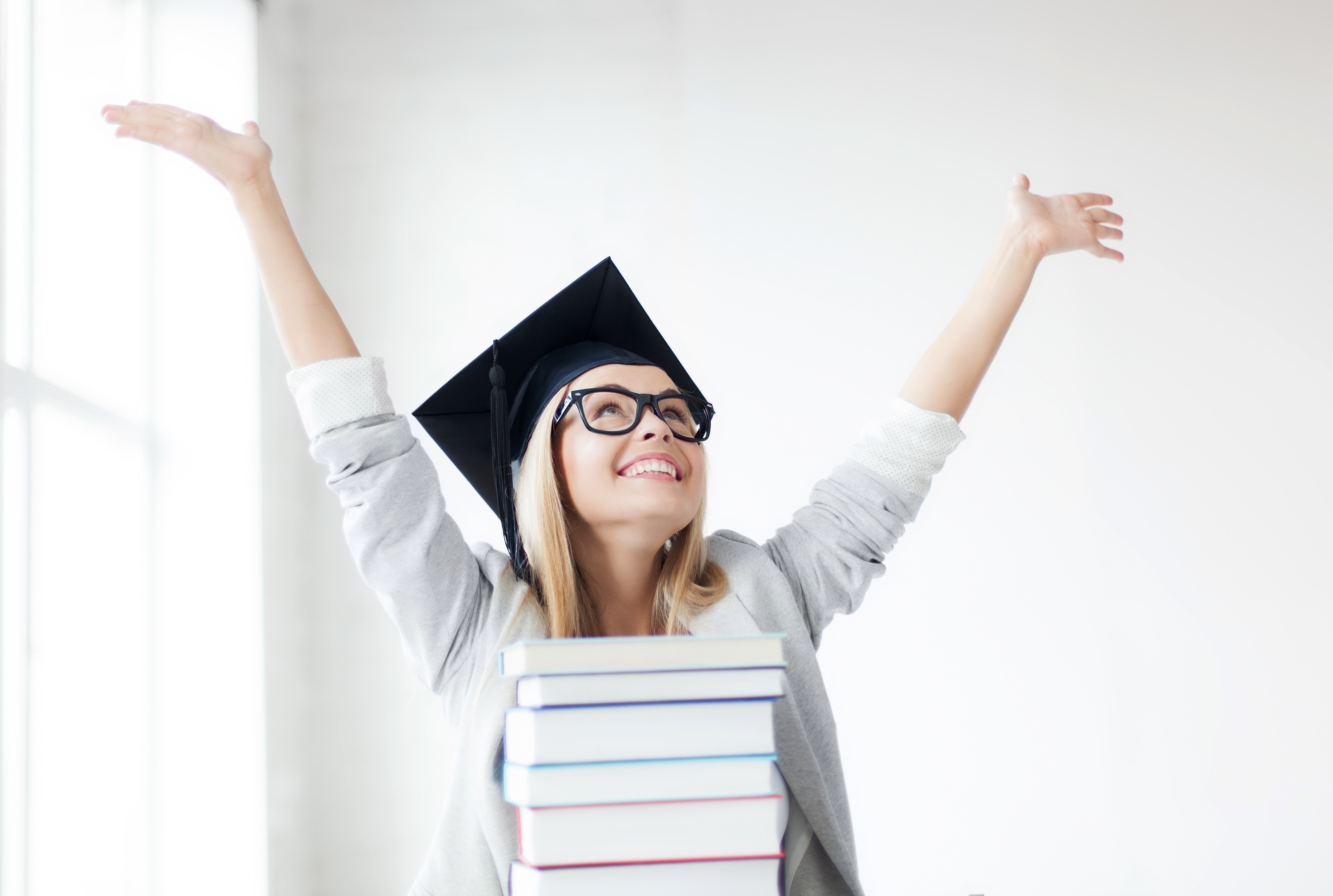 Élève heureuse portant un chapeau de graduation avec une pile de livres devant elle