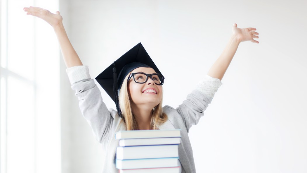 Élève heureuse portant un chapeau de graduation avec une pile de livres devant elle