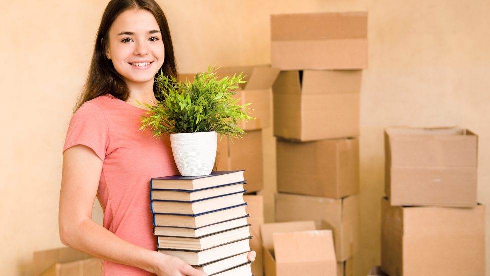 Jeune femme déménagement au collège, tenant des livres et des plantes