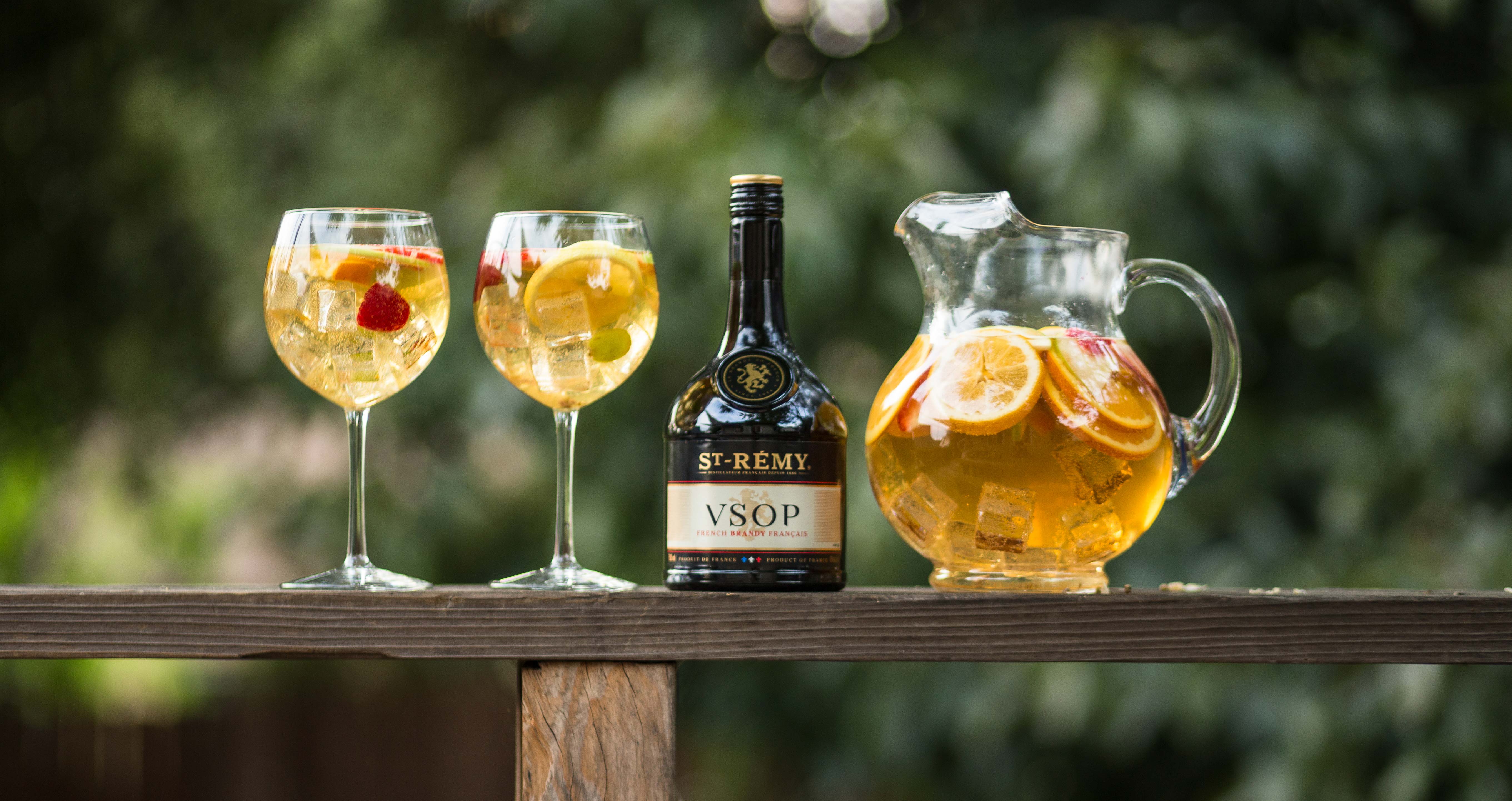 Un pichet de sangria avec deux coupes et une bouteille de st-rémy déposés sur une table