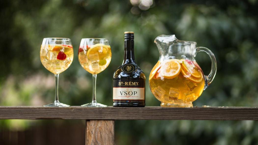 Un pichet de sangria avec deux coupes et une bouteille de st-rémy déposés sur une table