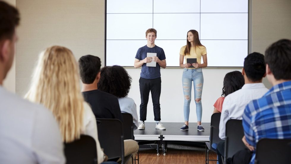 Students With Digital Tablets Giving Presentation To High School Class In Front Of Screen