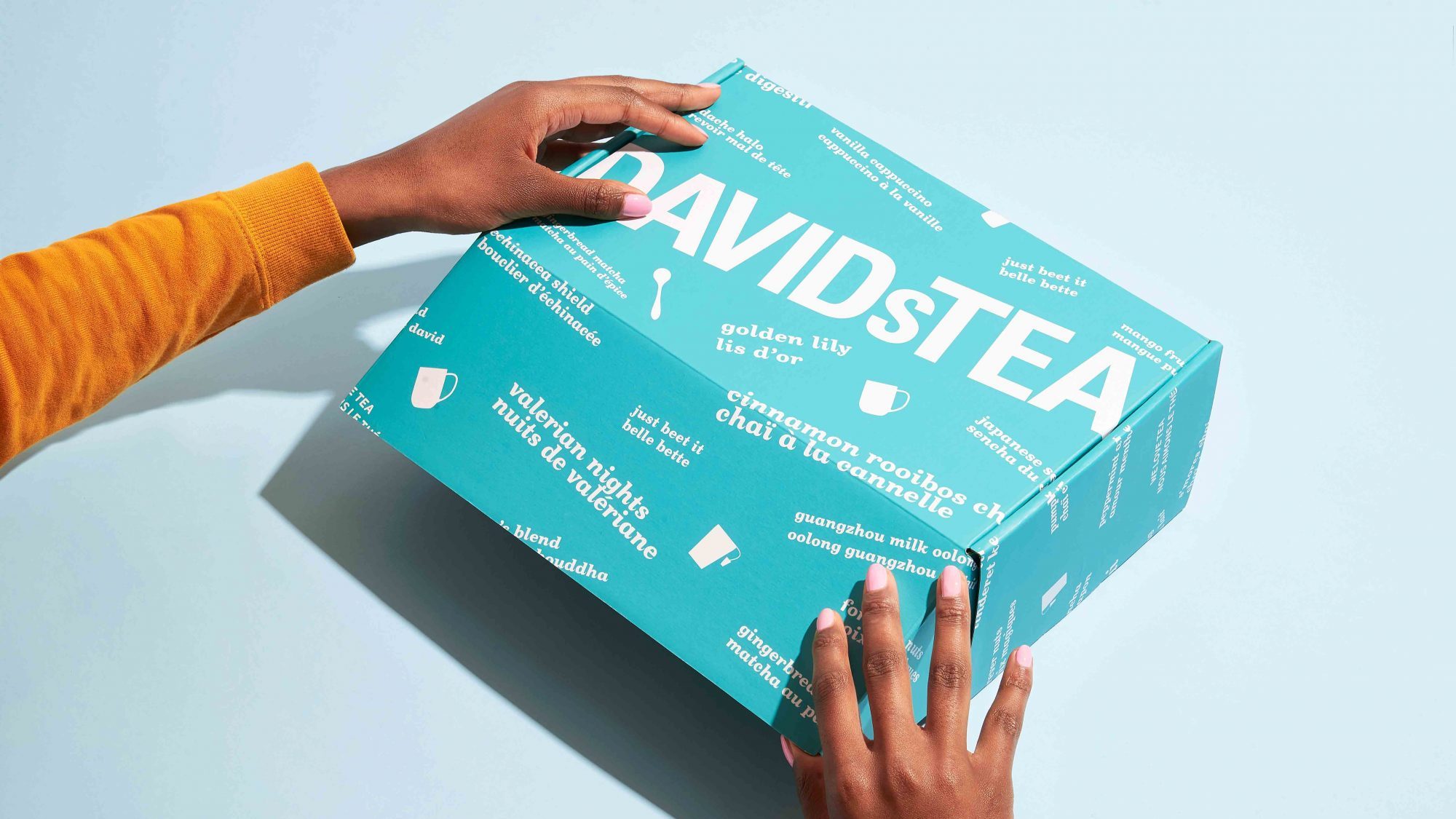 Des mains ouvrant une boîte de thé de couleur verte de la marque DAVIDs TEA