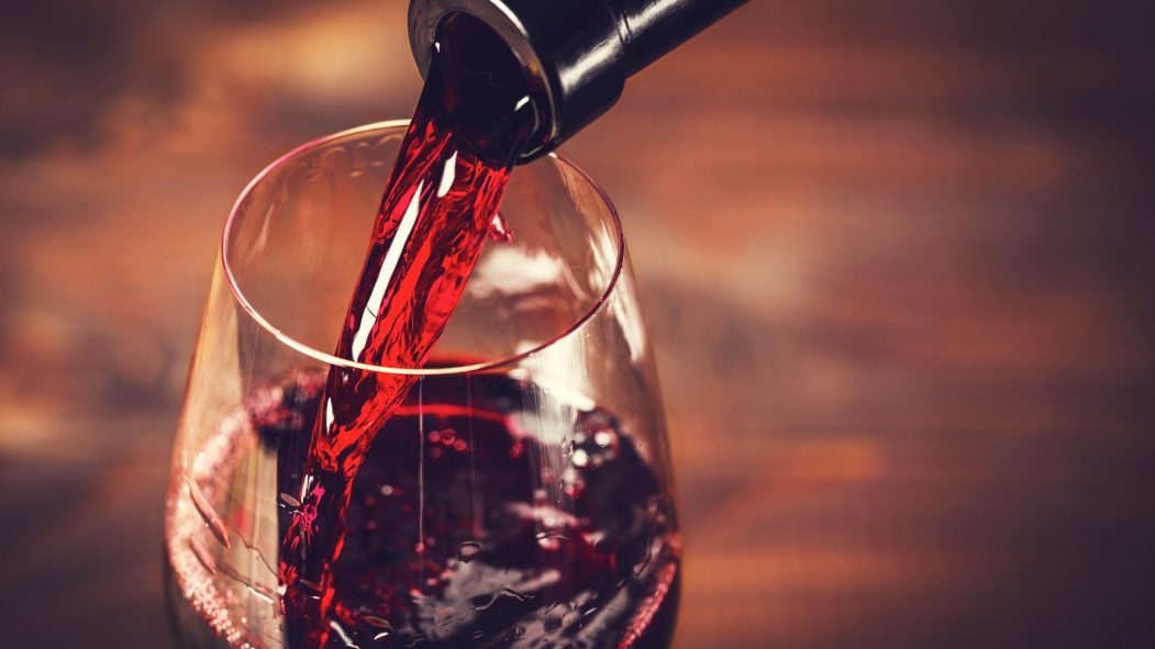 Pouring red wine into the glass against wooden background