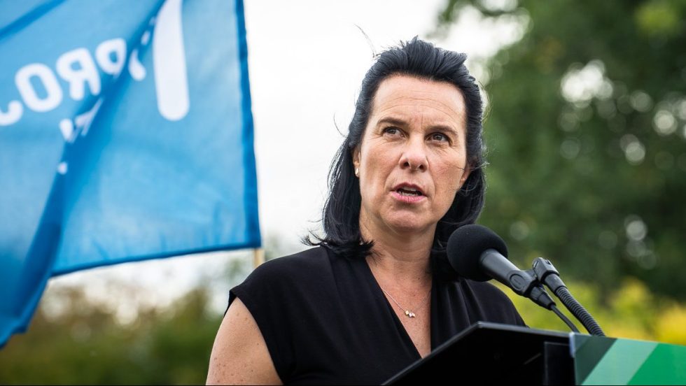 Valérie Plante devant un drapeau de Projet Montréal pendant une annonce sur le registre des loyers