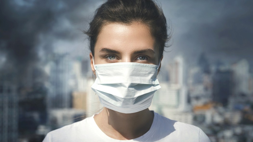 Une jeune femme portant un masque devant un environnement urbain marqué par le smog, la pollution et les gaz à effet de serre