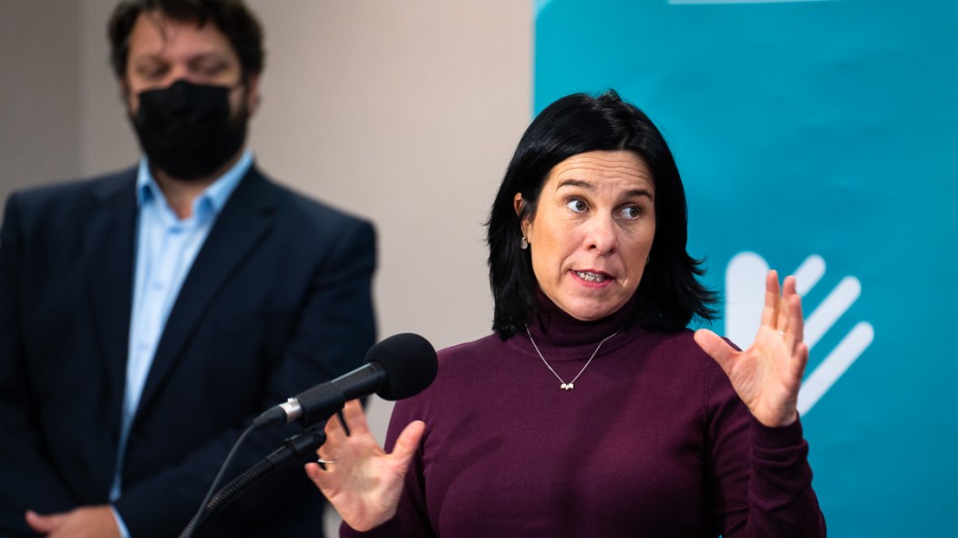 Valérie Plante devant une affiche de Projet Montréal lors d'une annonce concernant le logement à l'ancien hippodrome blue bonnets. En arrière-plan, Éric Alan Caldwell