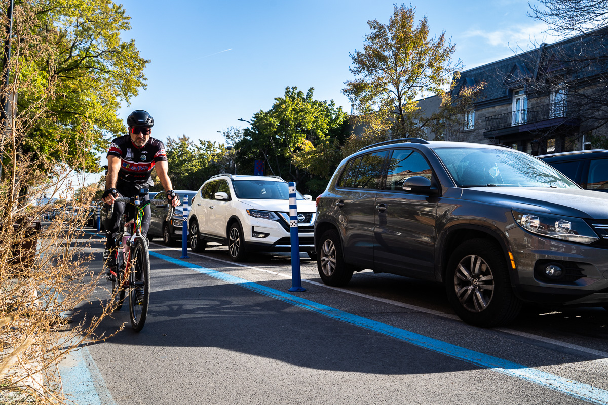 Un cycliste circule sur une piste cyclable près d'une série de VUS stationnés, alors qu'Équiterre demande une attaque frontale contre ce type de véhicule