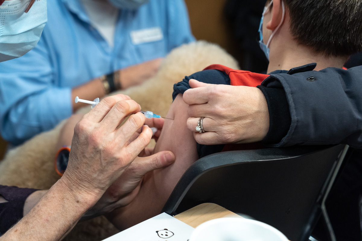 Un enfant reçoit une dose de vaccin contre la COVID-19 dans un centre de vaccination de Montréal, accompagné d'un chien.