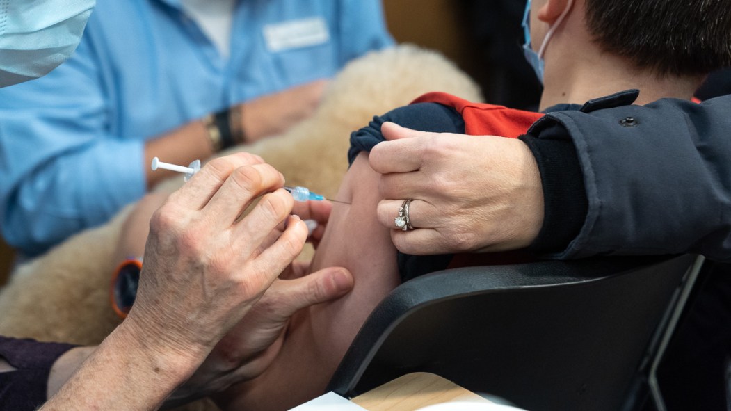 Un enfant reçoit une dose de vaccin contre la COVID-19 dans un centre de vaccination de Montréal, accompagné d'un chien.