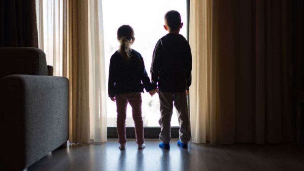 Les silhouettes de deux enfants se tiennent debout devant le portique d'un logement.