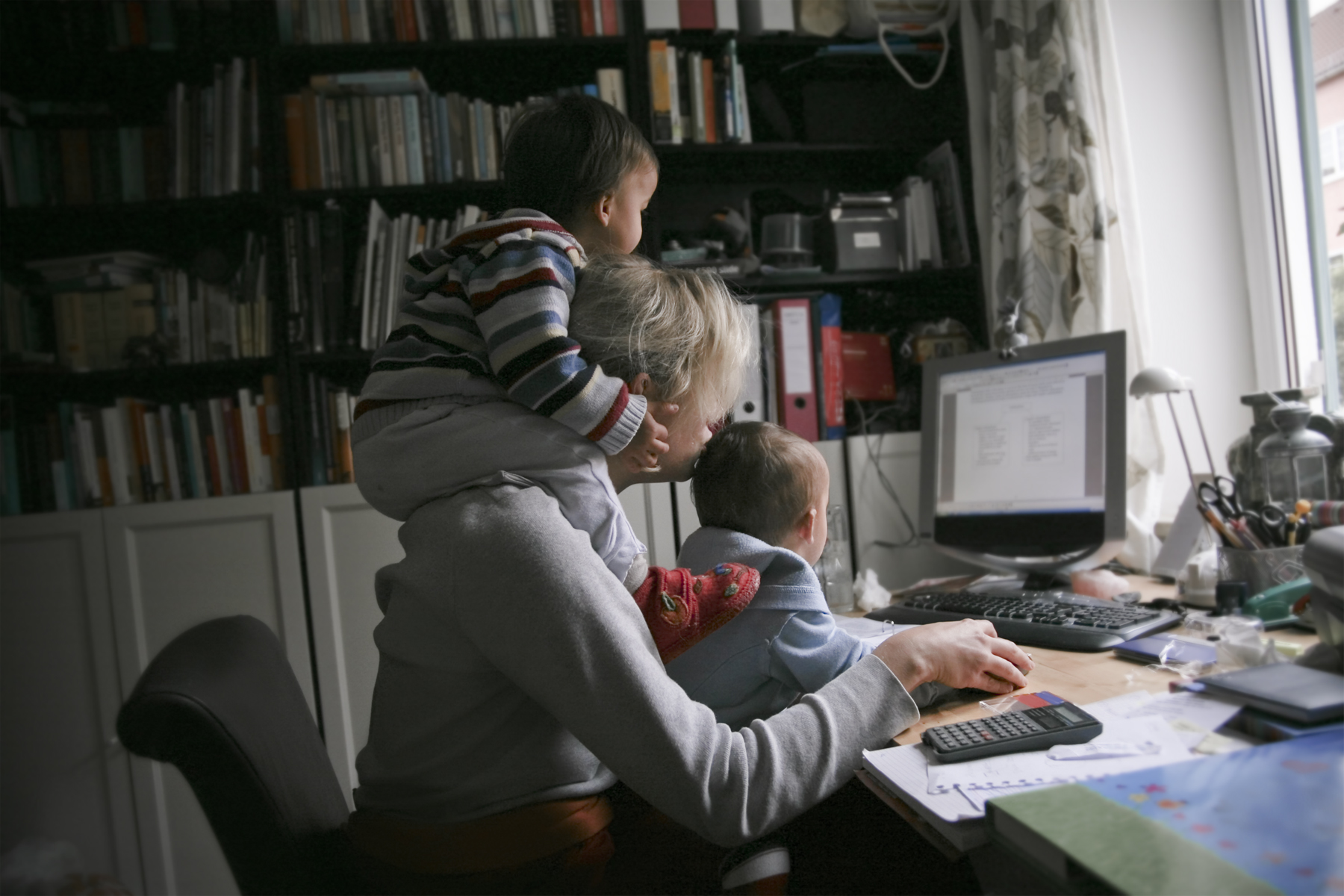 mère qui fait du télétravail avec ses deux enfants sur elle