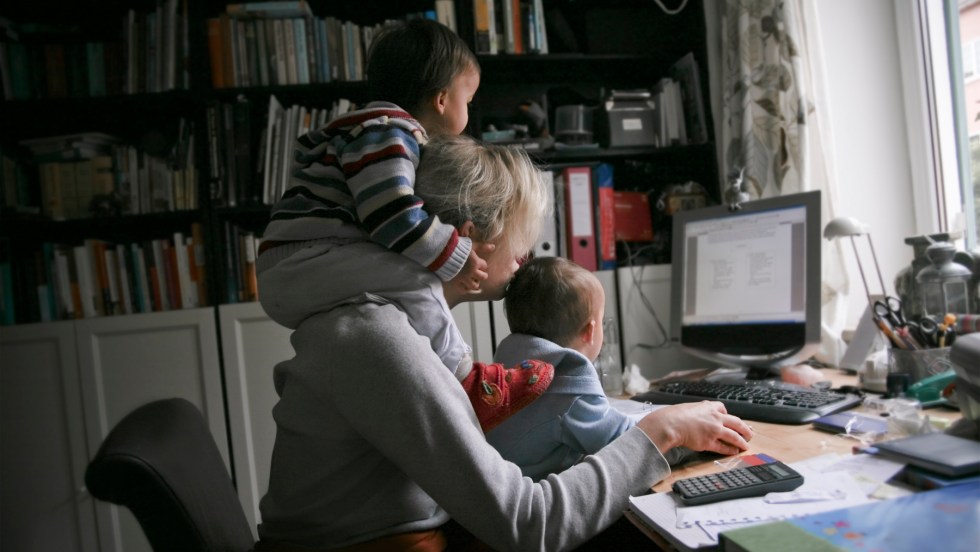 mère qui fait du télétravail avec ses deux enfants sur elle