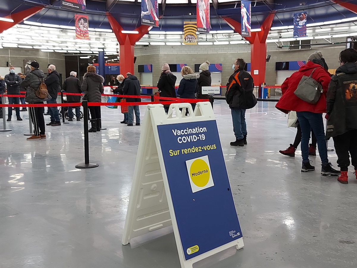 Des personnes de tous âges font la file à l'intérieur de la clinique de vaccination du Stade olympique de Montréal afin de recevoir leur troisième dose.