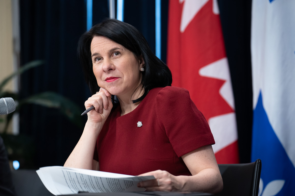 Valérie Plante, mairesse de Montréal, assise à un bureau devant les drapeaux du Canada et du Québec, lors de la présentation de la certification pour propriétaires de logements et du registre des loyers.