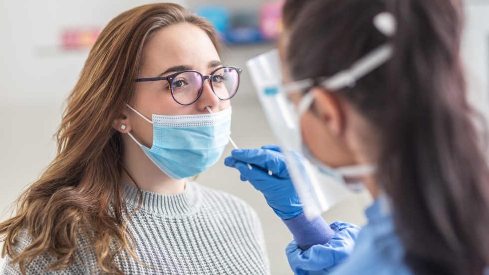 une jeune femme reçoit un test covid nasal par une infirmière en habit de protection contre le virus