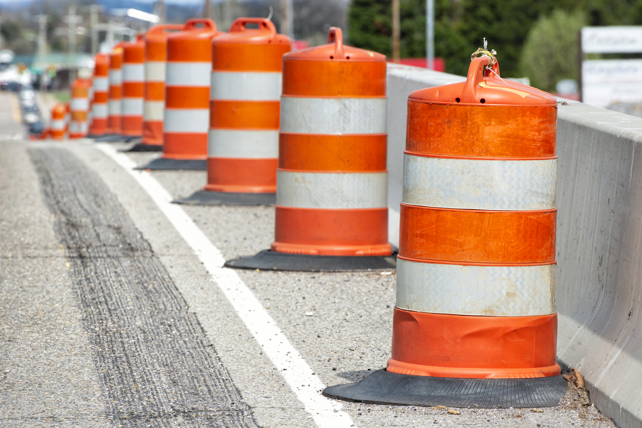 Horizontal close-up shot of orange and white striped traffic barrels down the side of a road with shallow depth of field.