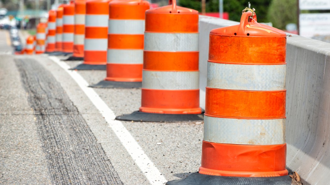 Horizontal close-up shot of orange and white striped traffic barrels down the side of a road with shallow depth of field.