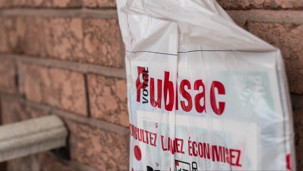 Un Publisac contenant des circulaires et des journaux locaux est accroché devant un mur de brique d'une résidence de Montréal.