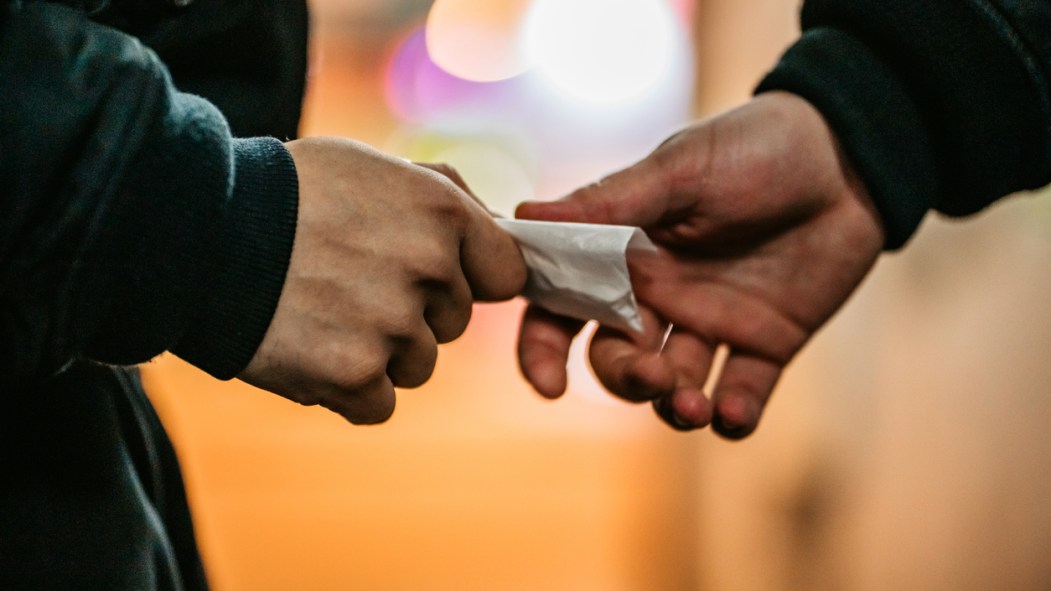 Vue rapprochée de deux mains. L'une, la main d'un trafiquant de drogue qui tend un sachet. L'autre, la main d'un client qui prend le sachet de drogue.