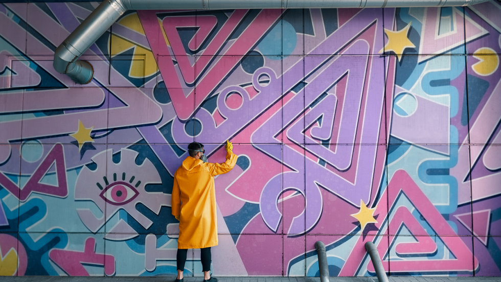 artiste de graffiti portant un manteau jaune et un masque, devant une murale