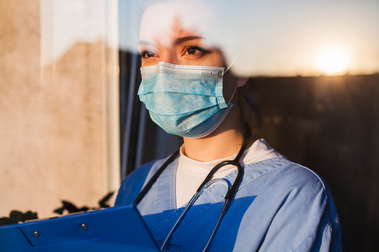 une infirmière à un air pensif et regarde à travers une fenêtre