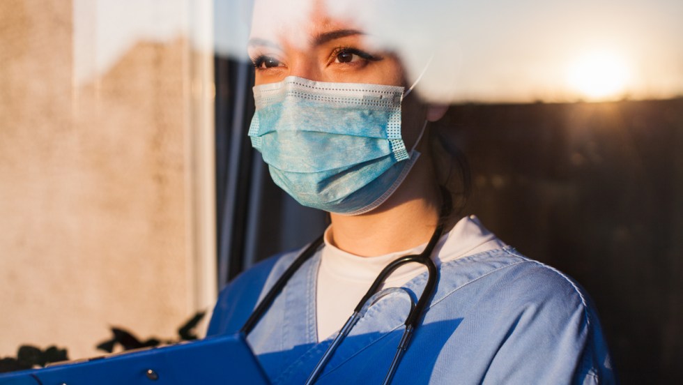 une infirmière à un air pensif et regarde à travers une fenêtre