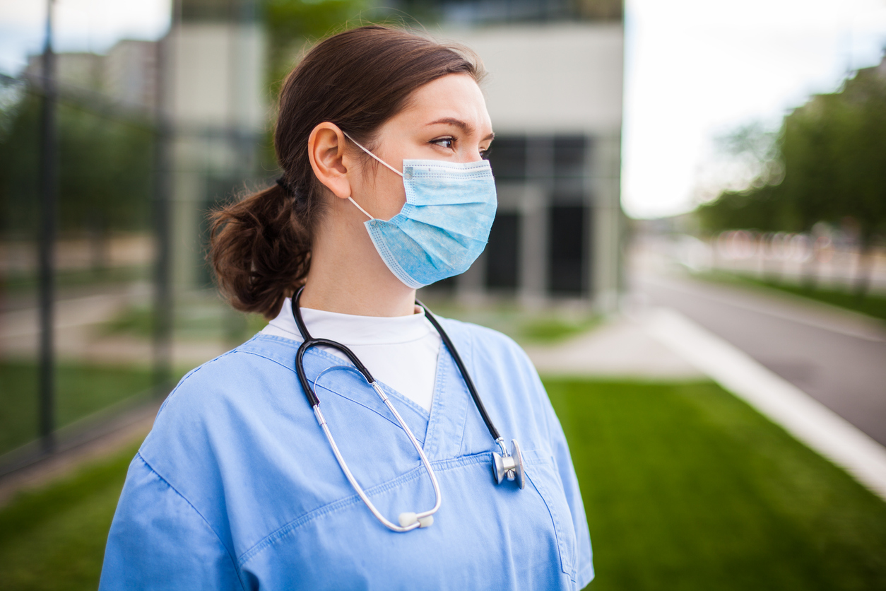 une infirmière portant un masque devant un hôpital semble inquiète