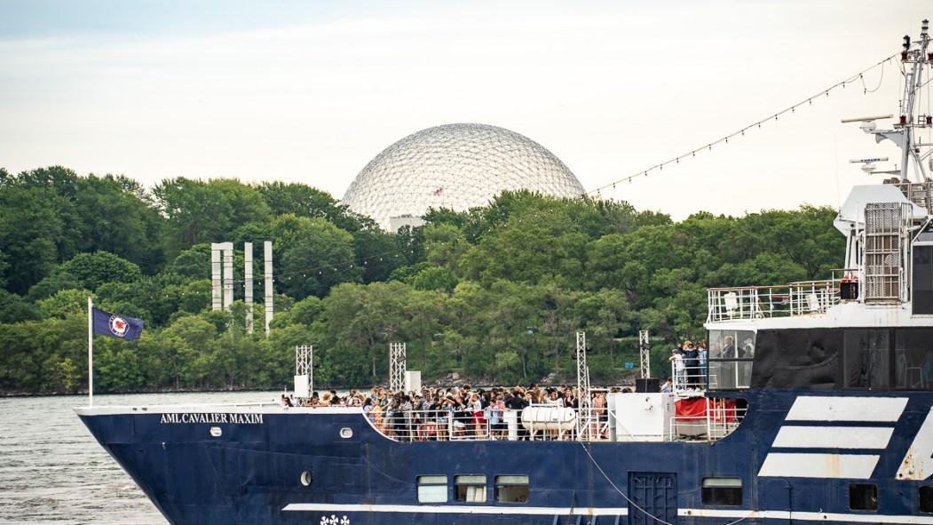 Un bateau de plaisance passe derrière des touristes dans le Vieux-Port de Montréal, devant le dôme de la Biosphère.