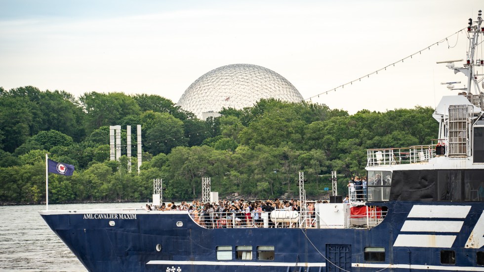 Un bateau de plaisance passe derrière des touristes dans le Vieux-Port de Montréal, devant le dôme de la Biosphère.