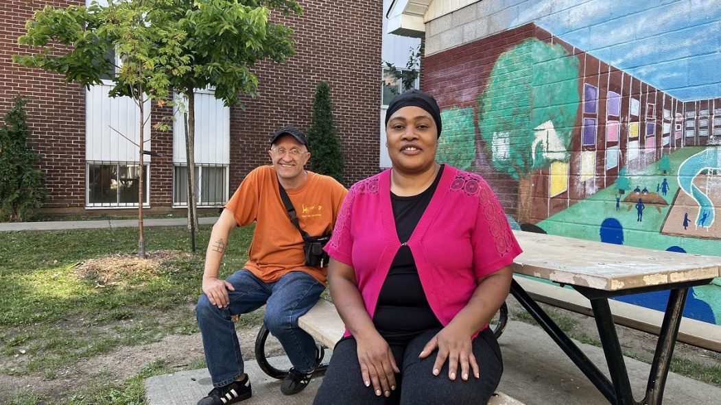 José Trottier et Guerda Calisthene assis sur une table, devant une murale