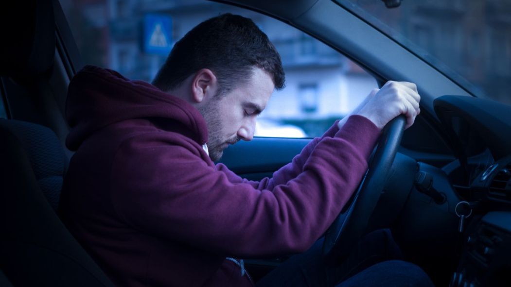 Un homme inquiet se penche sur le volant de sa voiture, symbolisant la face cachée de l'itinérance.