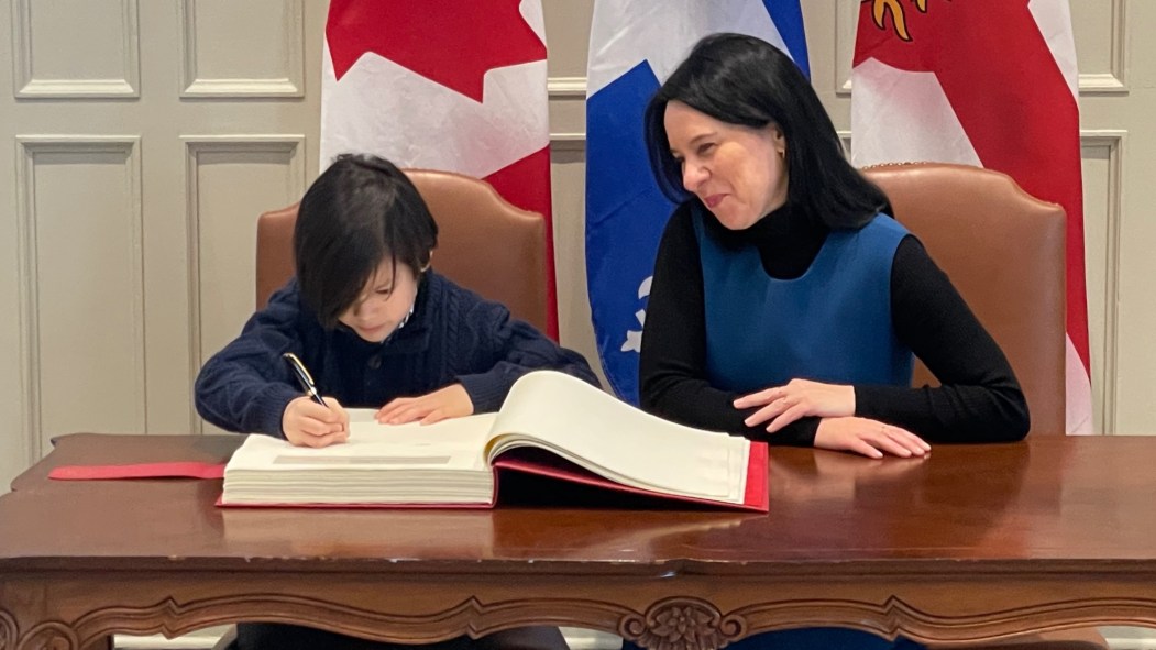 Le jeune Robert signe le livre d'or de la Ville de Montréal aux côtés de la mairesse Plante.